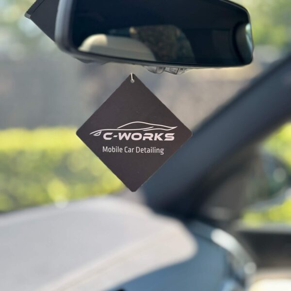 een close up van een geurhanger van C-Works Car Detailing die in een auto hangt